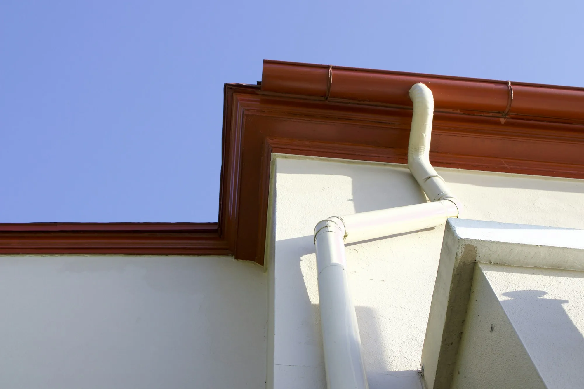 Copper-toned gutter and white downspout on a stucco wall