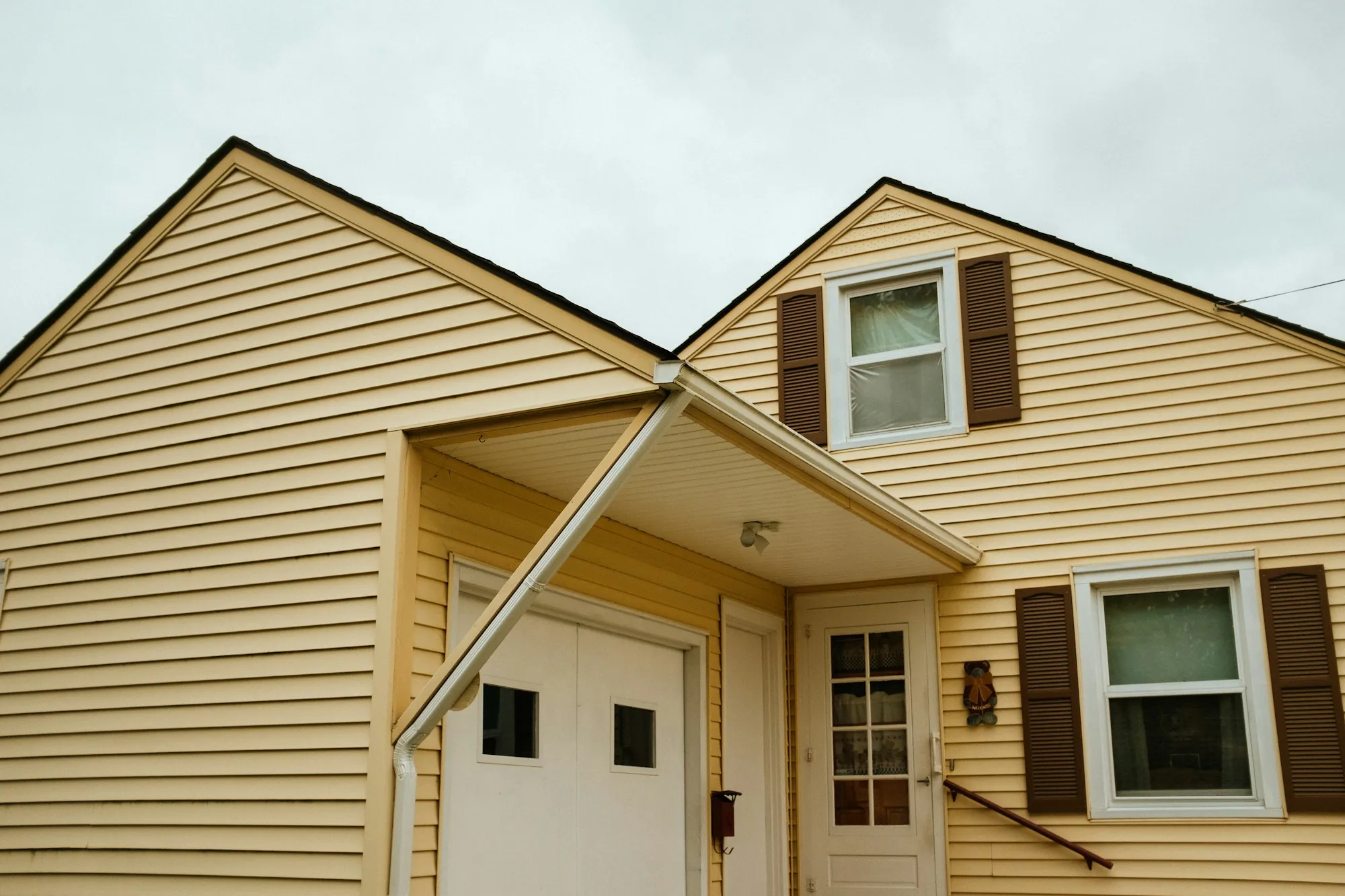 Yellow vinyl-sided house with a covered entry and shutters