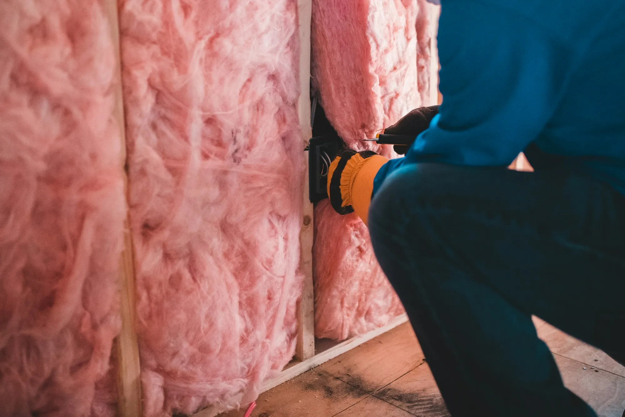 Gloved hand fitting pink insulation between wall studs, part of the home upkeep that goes with a regular roof inspection schedule in Clarkston